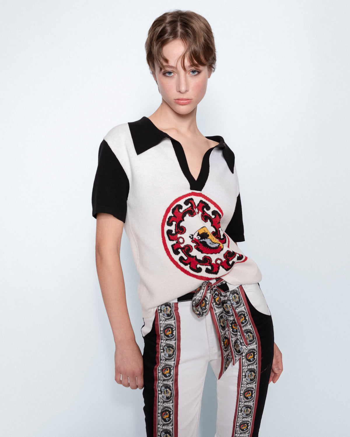 World On Fire Medallion Knit Black Polo worn with embroidered white jeans, close up