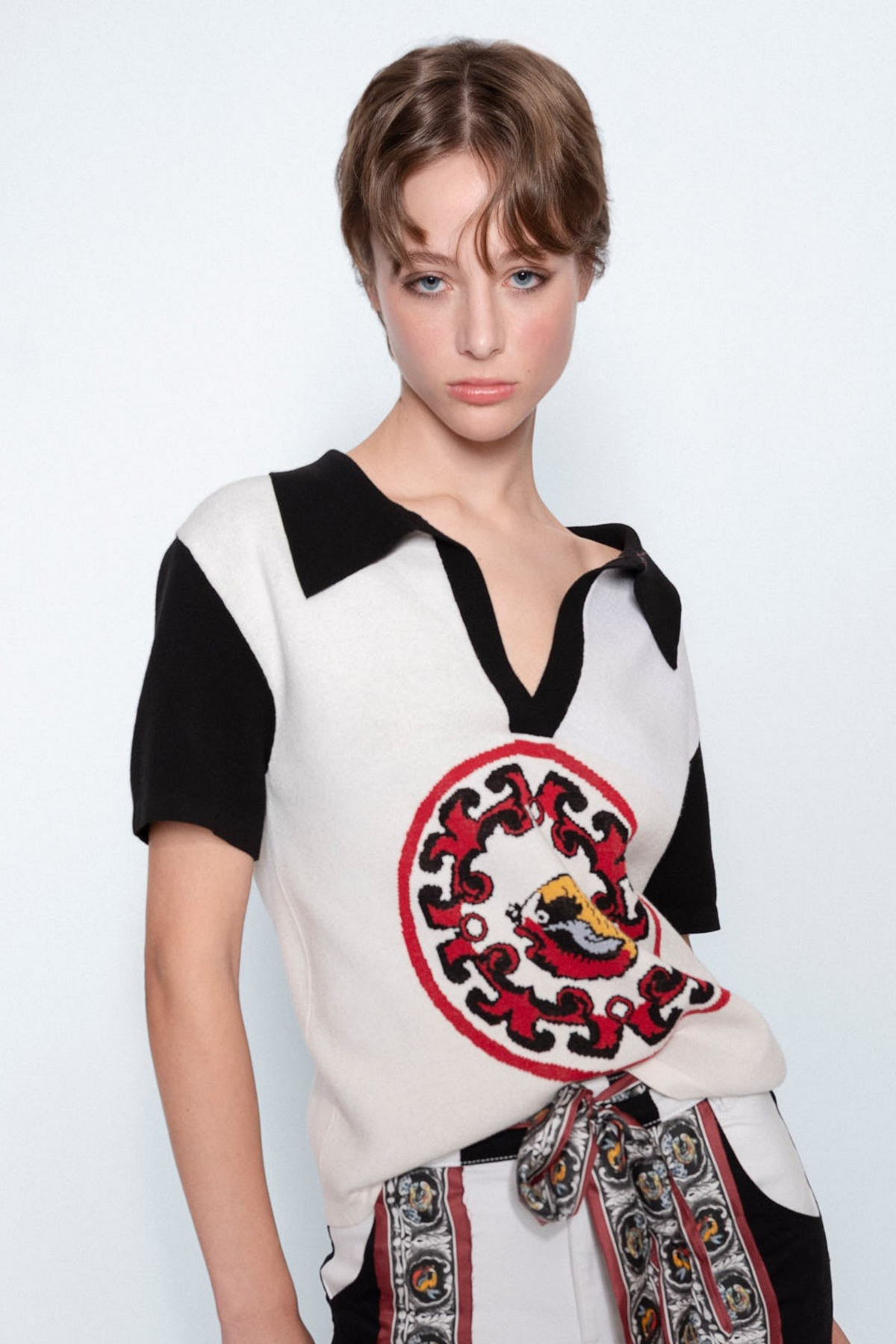 World On Fire Medallion Knit Black Polo worn with embroidered white jeans, close up